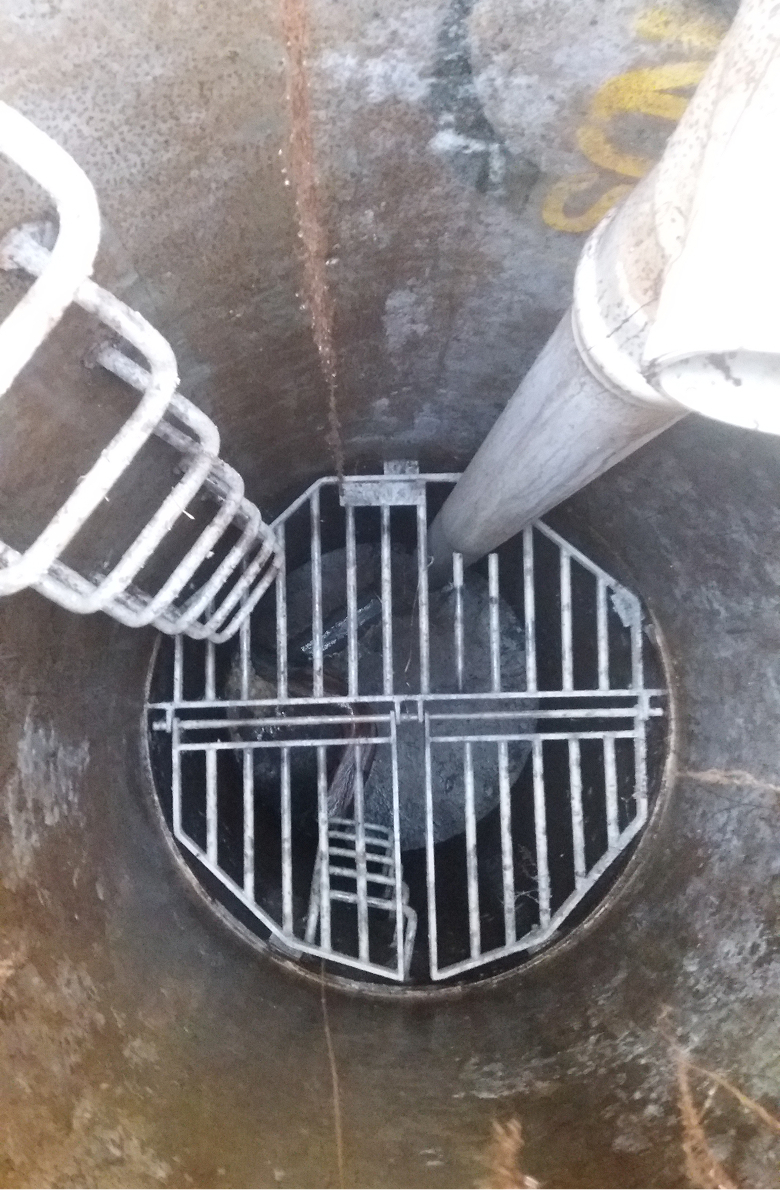 Top down look of a sewer, with a ladder & pipes.